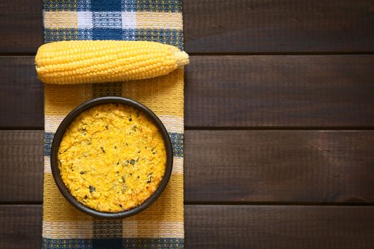 Overhead shot of traditional Chilean corn pie called Pastel de Choclo served in bowl, photographed on dark wood  with natural light. Below the corn-basil mix is ground meat, olive, boiled egg, raisins and pieces of chicken.   