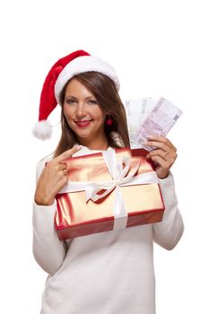 Vivacious beautiful young woman wearing a Santa hat with a large red Christmas gift and money, conceptual of successful Xmas shopping and payment, on white