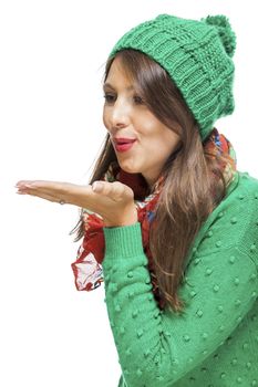 Romantic pretty young woman in a knitted green winter outfit blowing a kiss across the palm of her hand to her sweetheart or while flirting, isolated on white