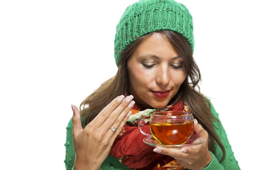 Attractive young woman in a trendy green knitted winter ensemble warming up with a cup of hot tea isolated on white