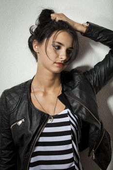 Pretty Young Woman in Black Leather Jacket Holding her Black Hair While Facing Right. Captured with Gray Wall Background.