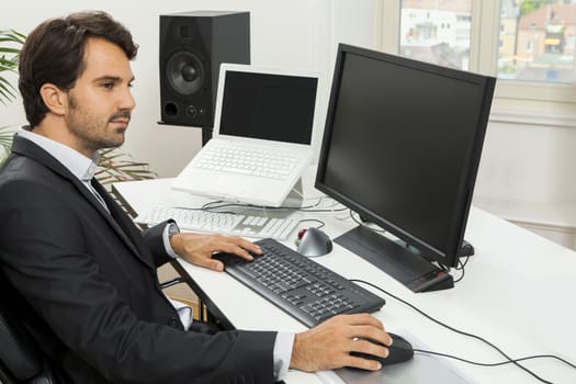 Stylish businessman in a suit sitting at his desk in the office chatting on the phone with a view of his blank computer monitor