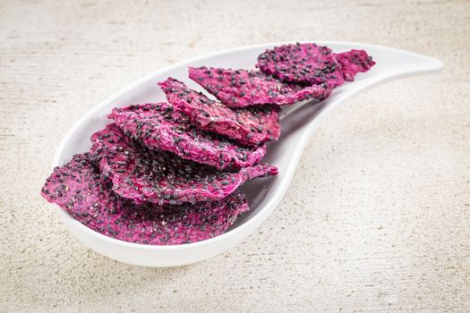 slices of dried red dragon fruit on a teardrop shaped bowl against rustic wood