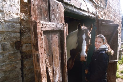caucasian teenage girl with her horse friend peeking from old wooden stable door