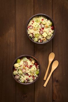 Overhead shot of two bowls of vegetarian couscous salad with grapes, pomegranate, walnuts, cheese, lime and mint, photographed with natural light