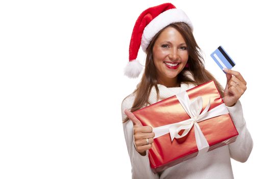 Smiling woman wearing a red Santa hat purchasing Christmas gifts on a bank card holding up a colorful red giftwrapped box with a happy smile and a thumbs up gesture of success, isolated on white