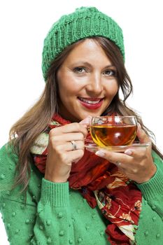 Attractive young woman in a trendy green knitted winter ensemble warming up with a cup of hot tea isolated on white