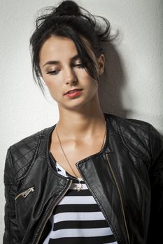 Pretty Young Woman in Black Leather Jacket Holding her Black Hair While Facing Right. Captured with Gray Wall Background.
