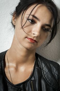 Pretty Young Woman in Black Leather Jacket Holding her Black Hair While Facing Right. Captured with Gray Wall Background.