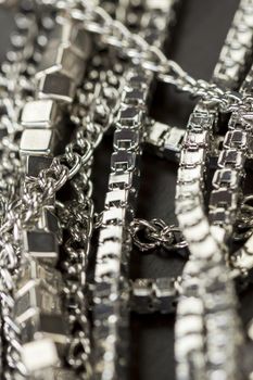 Pile of assorted silver chains with shiny box chains, cube chains and ordinary linked chain on a grey background conceptual of fashion jewellery