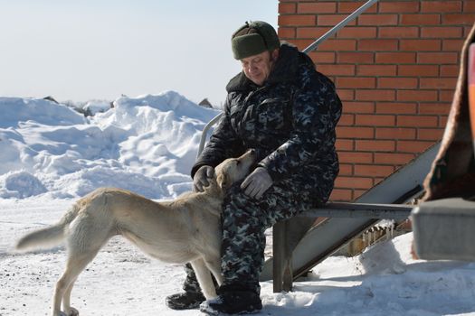 A man in camouflage clothing stroking dog