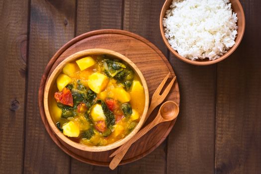 Overhead shot of pumpkin, mangold, potato and tomato curry dish in wooden bowl with rice, photographed with natural light