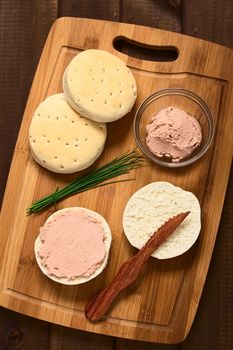 Overhead shot of liverwurst spread on bun with chives, knife and buns on wooden board, photographed with natural light