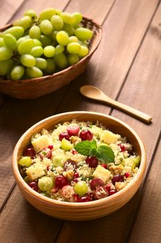 Vegetarian couscous salad with grapes, pomegranate, walnuts, cheese, lime and mint in wooden bowl photographed with natural light (Selective Focus, Focus on the mint leaf on the dish) 