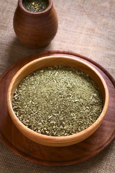 South American yerba mate (mate tea) dried leaves in wooden bowl with a wooden mate cup filled with tea photographed with natural light. Mate is the national infusion of Argentina. (Selective Focus, Focus one third into the dried tea) 