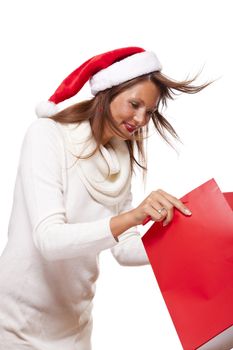 Happy vivacious Christmas shopper wearing a red Santa hat holding up a colorful red shopping bag with a beautiful beaming smile, isolated on white with copyspace