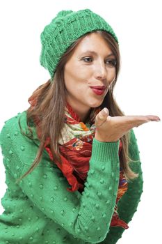 Romantic pretty young woman in a knitted green winter outfit blowing a kiss across the palm of her hand to her sweetheart or while flirting, isolated on white