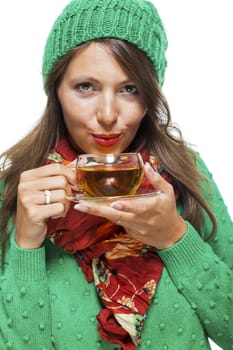 Attractive young woman in a trendy green knitted winter ensemble warming up with a cup of hot tea isolated on white