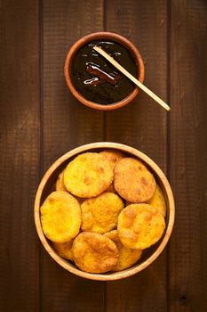 Overhead shot of traditional Chilean Sopaipilla fried pastry made with mashed pumpkin in the dough, served with Chancaca sweet sauce, photographed on wood with natural light