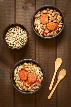 Overhead shot of traditional Chilean dish called Porotos con Riendas (English: beans with reins), made of cooked beans, linguine (flat spaghetti) and served with fried sausage, photographed on wood with natural light