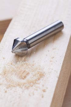 Battery operated hand drill standing amongst planks of new wood with a steel bit left protruding from a board in a concept of DIY, carpentry or joinery