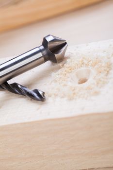 Battery operated hand drill standing amongst planks of new wood with a steel bit left protruding from a board in a concept of DIY, carpentry or joinery