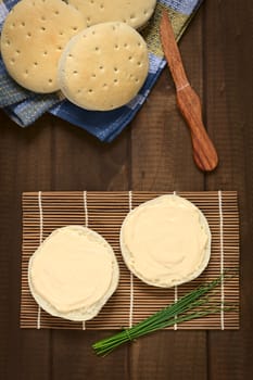 Overhead shot of cream cheese spread on bun with a bundle of chives on the side, photographed with natural light 