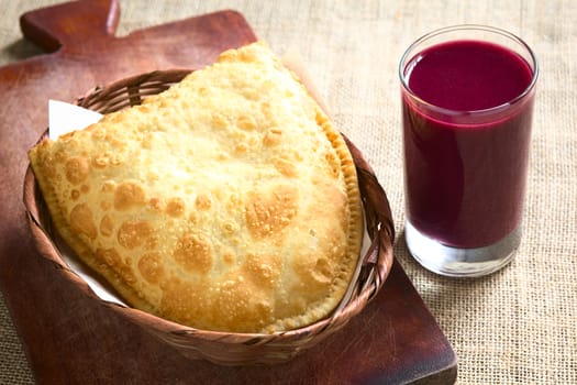 Traditional Bolivian snack called Pastel (deep-fried pastry filled with cheese) served with Api, a purple corn beverage, photographed with natural light (Selective Focus, Focus on the front of the pastry and the glass)