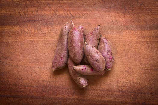 Overhead shot of raw purple sweet potato (lat. Ipomoea batatas) on wooden board photographed with natural light  