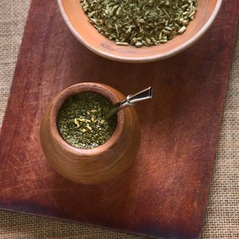 South American yerba mate tea in a wooden mate cup with strainer called bombilla, photographed with natural light. Mate is the national infusion of Argentina. (Selective Focus, Focus on the tea in the cup) 
