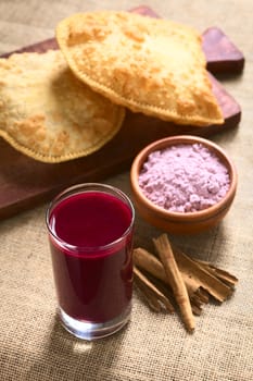 Traditional Bolivian Api, a purple corn beverage, with pastel (deep-fried pastry filled with cheese) in the back, photographed with natural light (Selective Focus, Focus in the middle of the drink's surface)