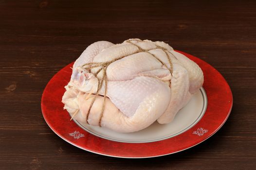 Bondage shibari raw chicken on red boarder plate on dark wood background horizontal