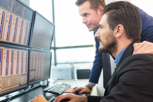 Businessmen trading stocks. Stock traders looking at graphs, indexes and numbers on multiple computer screens. Colleagues in discussion in traders office. 