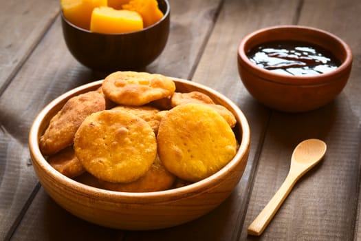 Traditional Chilean Sopaipilla fried pastry made with mashed pumpkin in the dough, served with Chancaca sweet sauce, photographed on wood with natural light (Selective Focus, Focus on the first two sopaipillas)