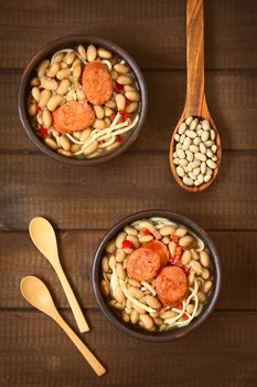 Overhead shot of traditional Chilean dish called Porotos con Riendas (English: beans with reins), made of cooked beans, linguine (flat spaghetti) and served with fried sausage, photographed on wood with natural light