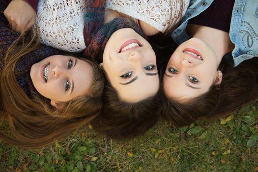 Trio of happy teenage girls laying down on grass