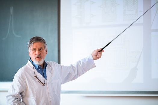 Senior chemistry professor giving a lecture in front of classroom full of students (shallow DOF; color toned image)