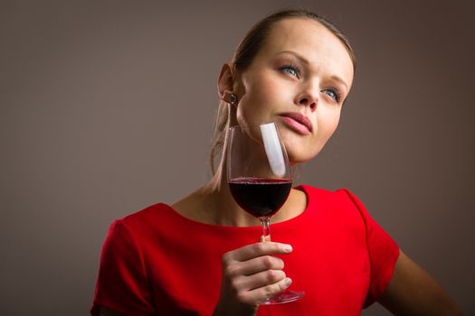 Elegant young woman in a red dress, having a glass of red wine