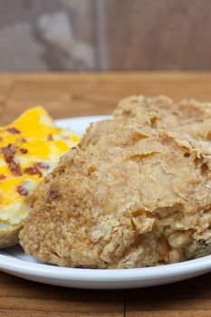 Crispy fried chicken on a plate with a twice baked potato with cheese and bacon.