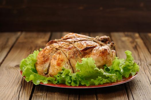 Bondage shibari roasted chicken with salad leaves on red plate on wooden background with dark space vertical