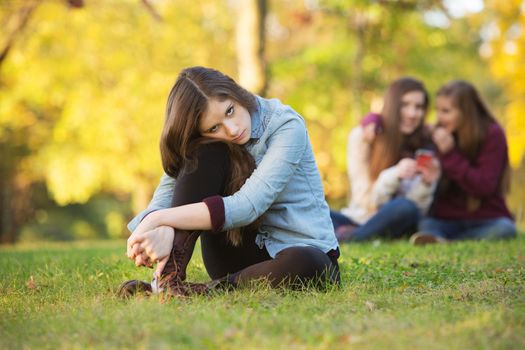 Lonely girl leaning on knee in front of teenagers talking