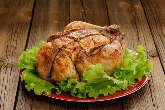 Bondage shibari roasted chicken with salad leaves on red plate on wooden background closeup horizontal