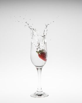 Strawberry falls deeply under water with a splash on white background