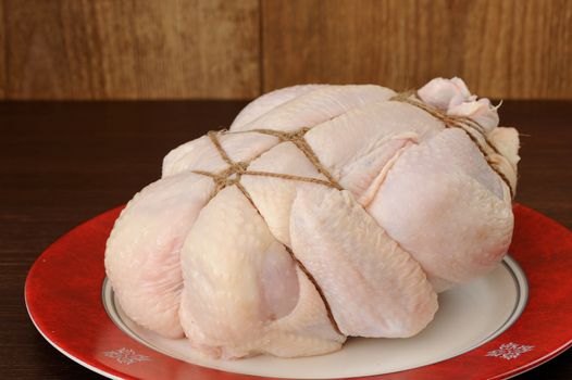 Bondage shibari raw chicken on red boarder plate on dark wood background horizontal