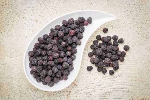 Dried chokeberry (aronia berry) in a teardrop shaped bowl against rustic barn wood