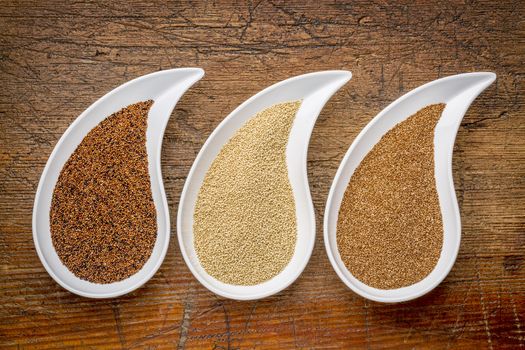 three tiny gluten free grains - kaniwa, amaranth and teff on teardrop shaped bowls against rustic wood