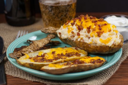 A twice baked potato, potato skins, and baked potato peals with a beer and sour cream in the background.