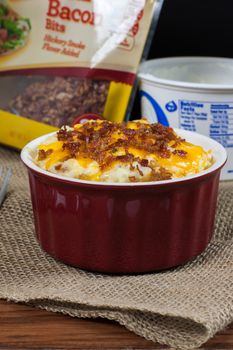 A crock of loaded mashed potatoes with melted cheese and bacon on top.
