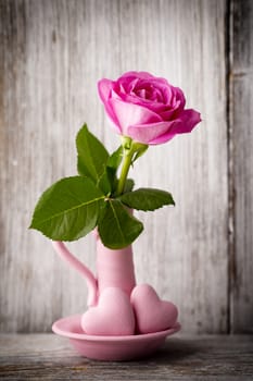 Pink roses in a vase with a Valentine's Day decoration on a wooden shelf.