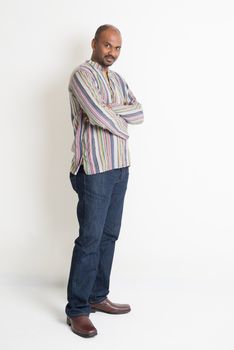 Full body Asian Indian guy in casual wear crossed arms standing on plain background with shadow.